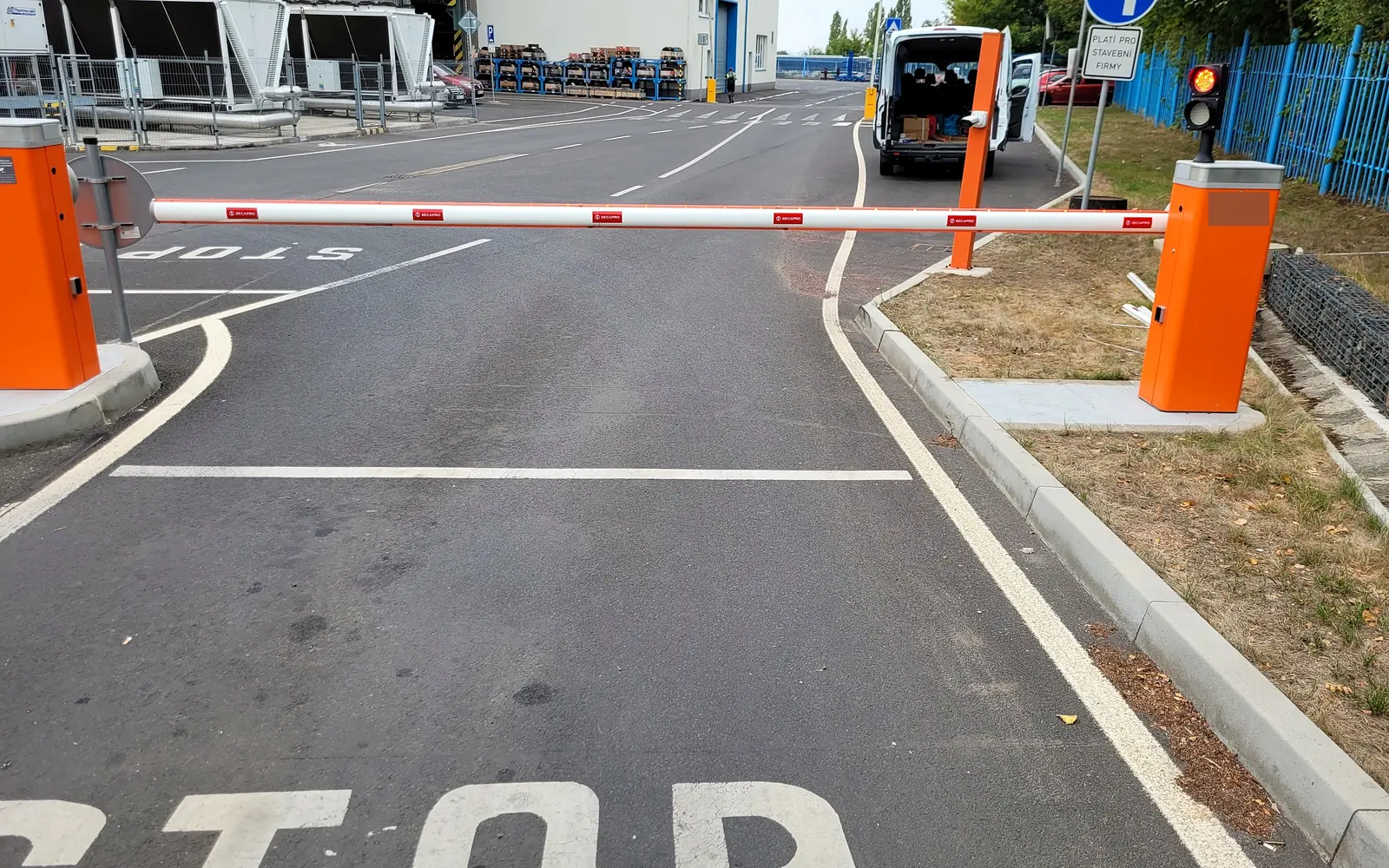 Dvě závory na vjezdu do výrobního areálu se semaforem a značením STOP