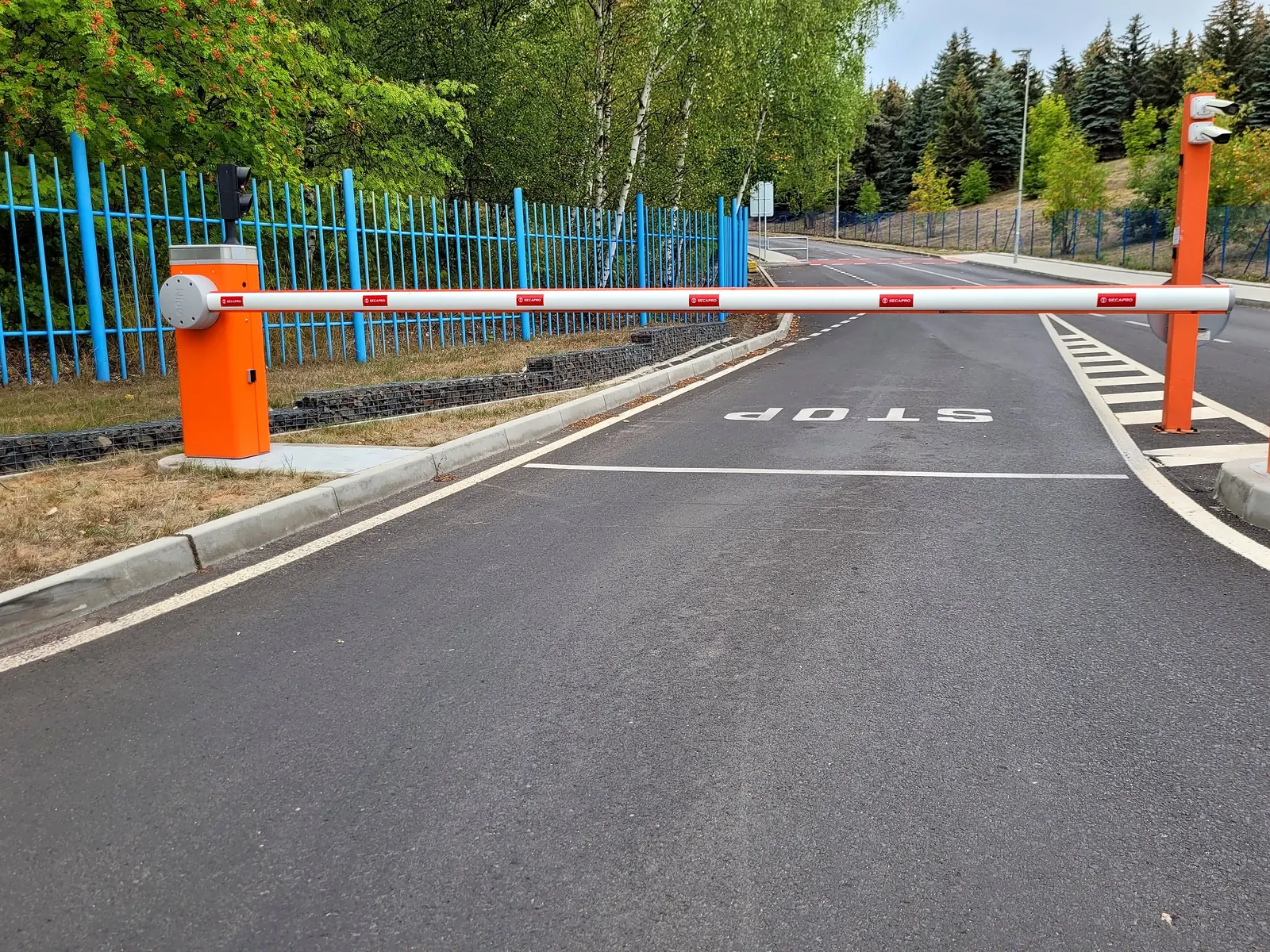 Vjezd do areálu se závorou, sloupem s kamerou pro čtení registrační značky a semaforem